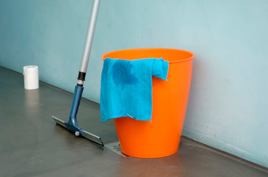 Two professional cleaning staff members from Islington Carpet Cleaning are standing indoors against a plain white wall, dressed in beige uniforms with short sleeves and badges. One is holding a vacuum